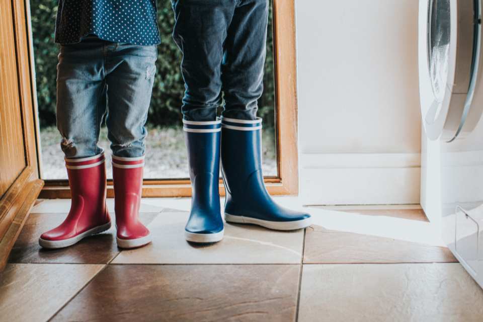 two kids walking in rain boots on tile floors in entryway with laundry machine